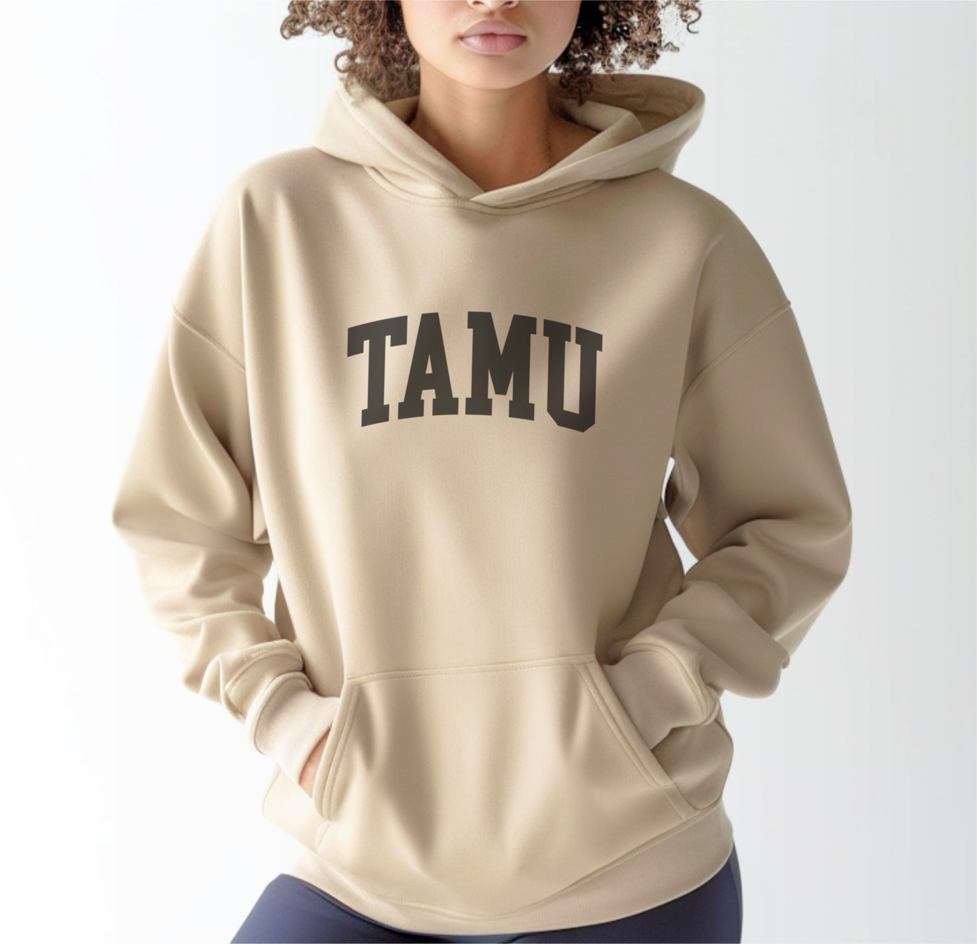 A model wears the Sand Adult Unisex Texas A&M TAMU Hooded Sweatshirt.  The ﻿Texas A&M TAMU﻿ graphic is in bold Black in a Collegiate style.