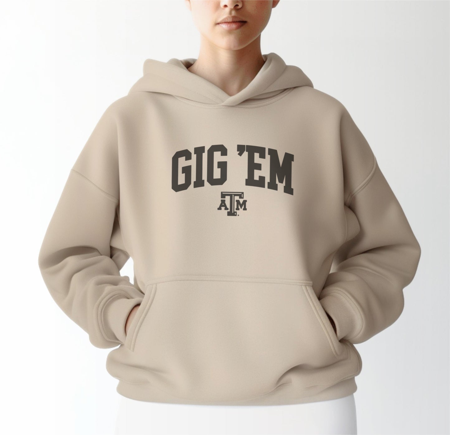 A model wears the Sand Adult Unisex Texas A&M Gig 'Em Collegiate Hooded Sweatshirt.  The ﻿Texas A&M Gig 'Em Collegiate﻿ graphic is in bold Black in a Collegiate style.