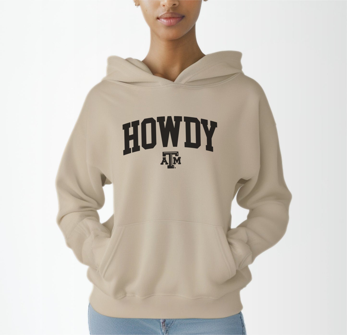 A model wears the Sand Adult Unisex Texas A&M Howdy Varsity Hooded Sweatshirt.  The ﻿Texas A&M Howdy Varsity﻿ graphic is in bold Black in a Collegiate style.