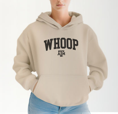 A model wears the Sand Adult Unisex Texas A&M Whoop Collegiate Hooded Sweatshirt.  The ﻿Texas A&M Whoop Collegiate﻿ graphic is in bold Black in a Varsity style.