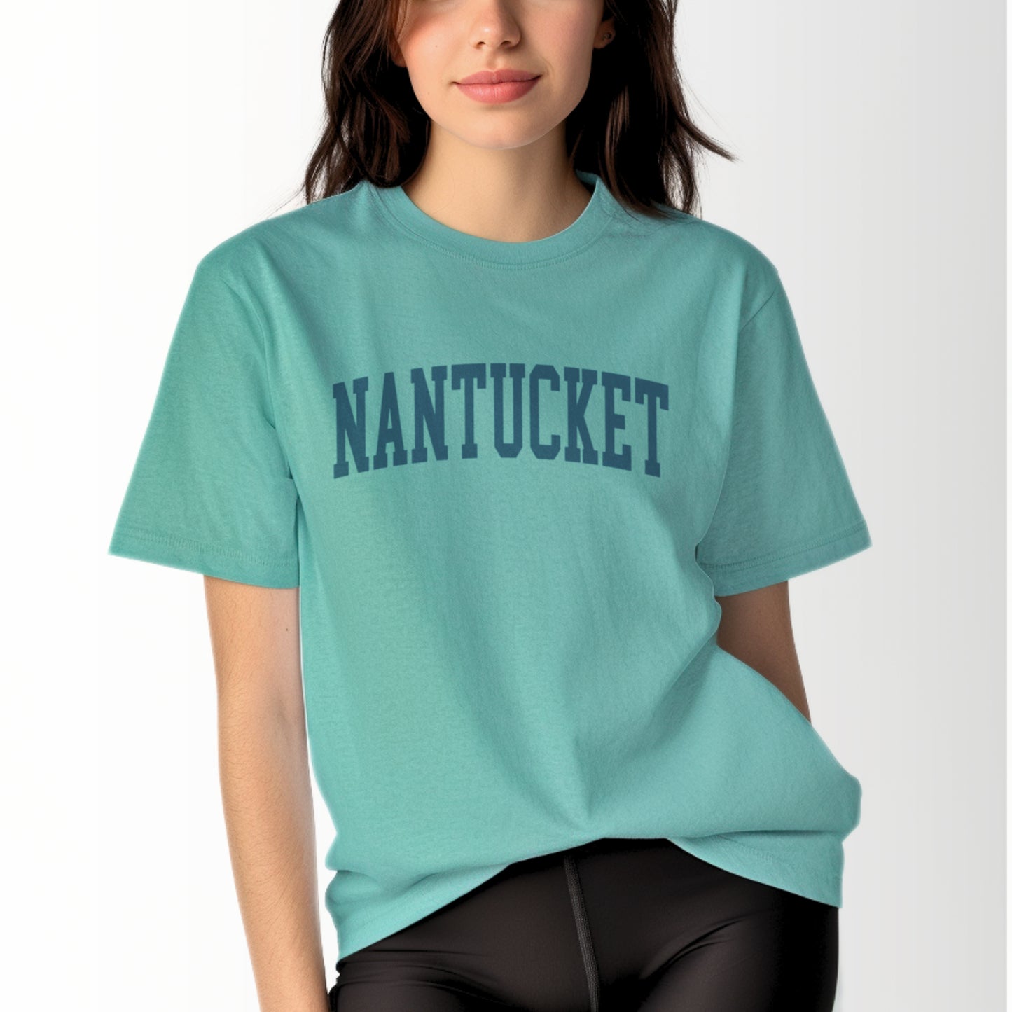 A model wears the Seafoam Adult Unisex Nantucket Massachusetts Varsity Comfort Colors T-shirt.  The ﻿Nantucket Massachusetts Varsity﻿ graphic is in bold Navy in a Collegiate Block style.