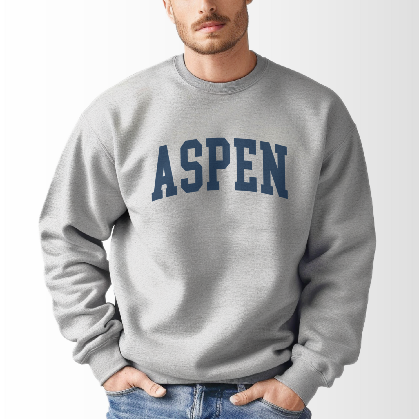 A model wears the Sport Grey Aspen Colorado Varsity Crewneck Sweatshirt.  The ﻿Aspen Colorado Varsity﻿ graphic is in bold Navy in a Collegiate style.