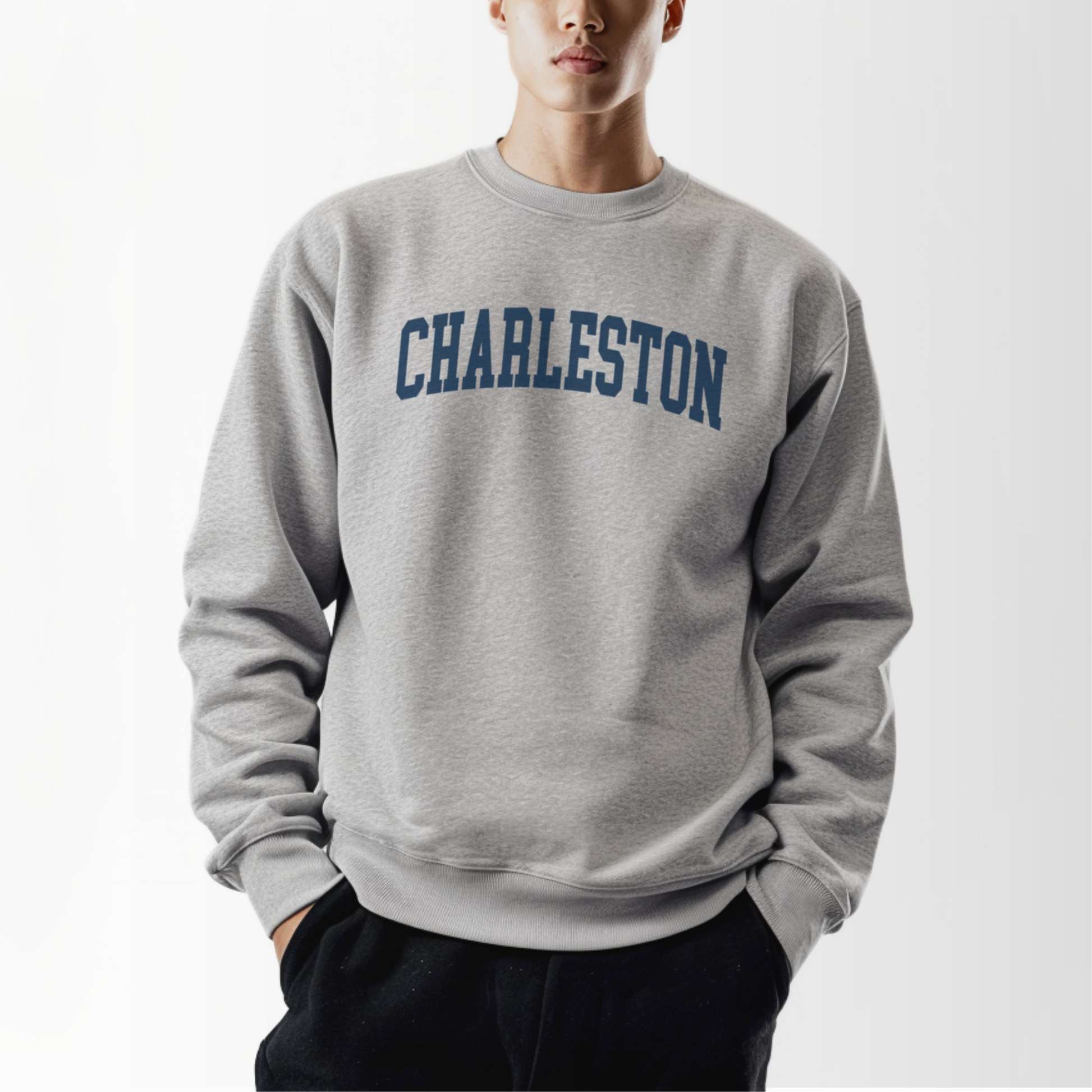 A model wears the Sport Grey Adult Unisex Charleston SC Collegiate Crewneck Sweatshirt.  The ﻿Charleston SC Collegiate﻿ graphic is in bold Navy in a Varsity style.