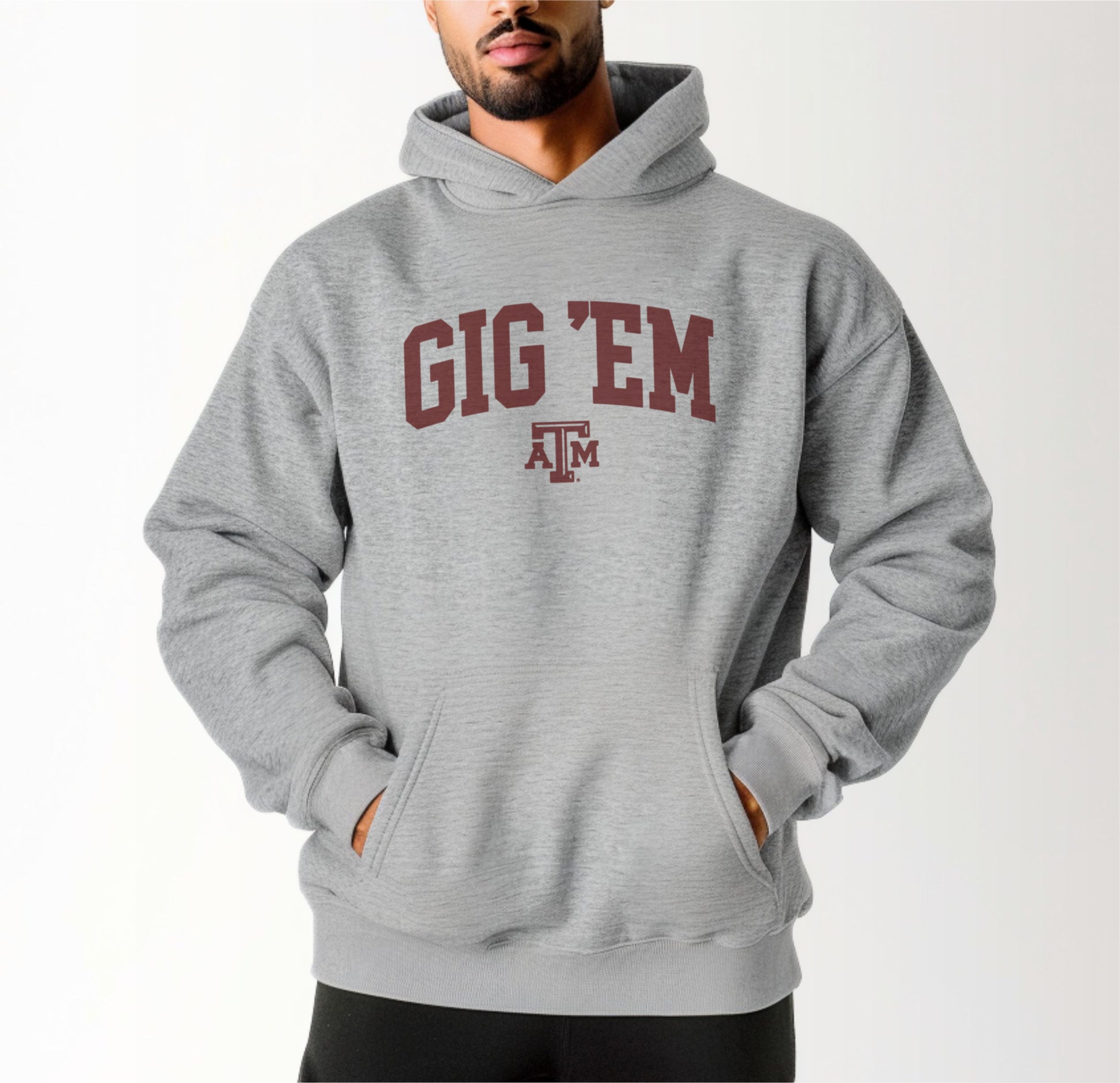 A model wears the Sport Grey Adult Unisex Texas A&M Gig 'Em Collegiate Hooded Sweatshirt.  The ﻿Texas A&M Gig 'Em Collegiate﻿ graphic is in bold Maroon in a Collegiate style.