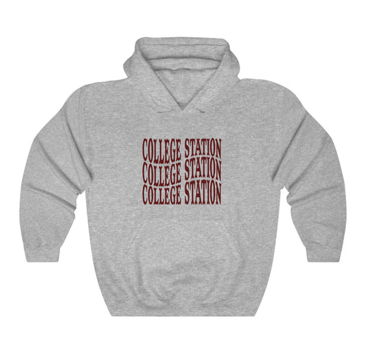 The Sport Grey Adult Unisex College Station Western Hooded Sweatshirt lays flat on a white background. The ﻿College Station Western﻿ graphic is in bold Maroon in a Western style.