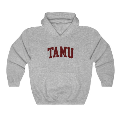 The Sport Grey Adult Unisex Texas A&M TAMU Hooded Sweatshirt lays flat on a white background. The ﻿Texas A&M TAMU﻿ graphic is in bold Maroon in a Collegiate style.