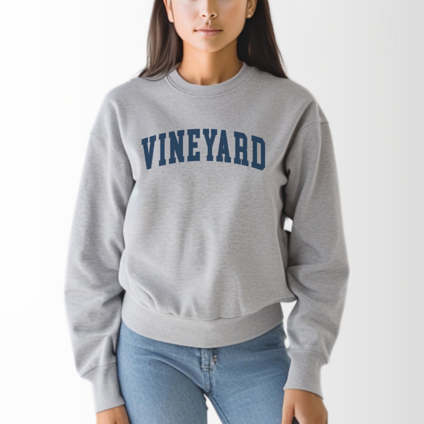 A model wears the Sport Grey Adult Unisex Martha's Vineyard Massachusetts Classic Crewneck Sweatshirt.  The ﻿Martha's Vineyard Massachusetts Classic﻿ graphic is in bold Navy in a Varsity style.