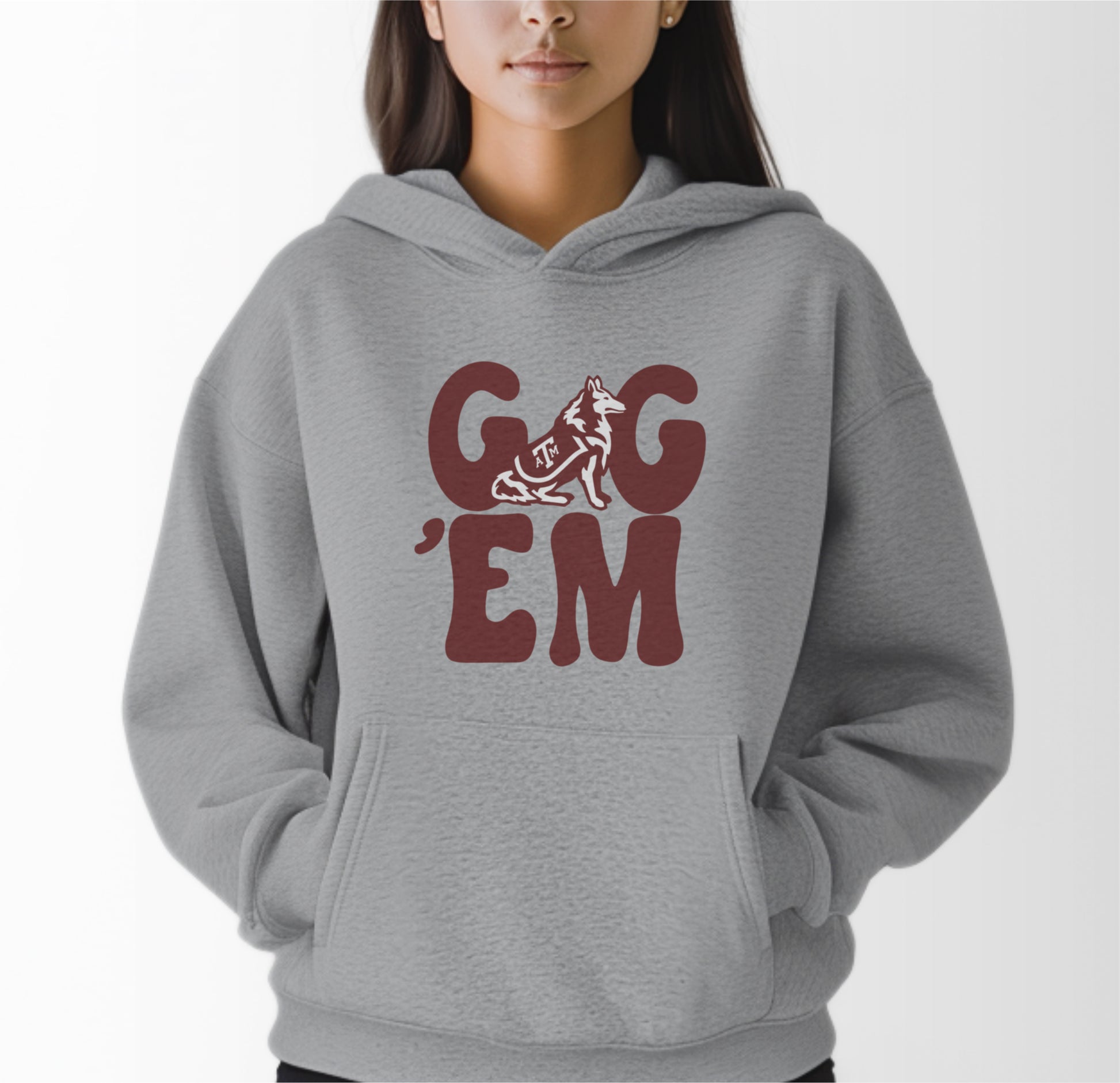 A model wears the Sport Grey Adult Unisex Texas A&M Gig 'Em Retro Reveille Hooded Sweatshirt.  The ﻿Texas A&M Gig 'Em Retro Reveille﻿ graphic is in bold Maroon in a Groovy Vintage style.