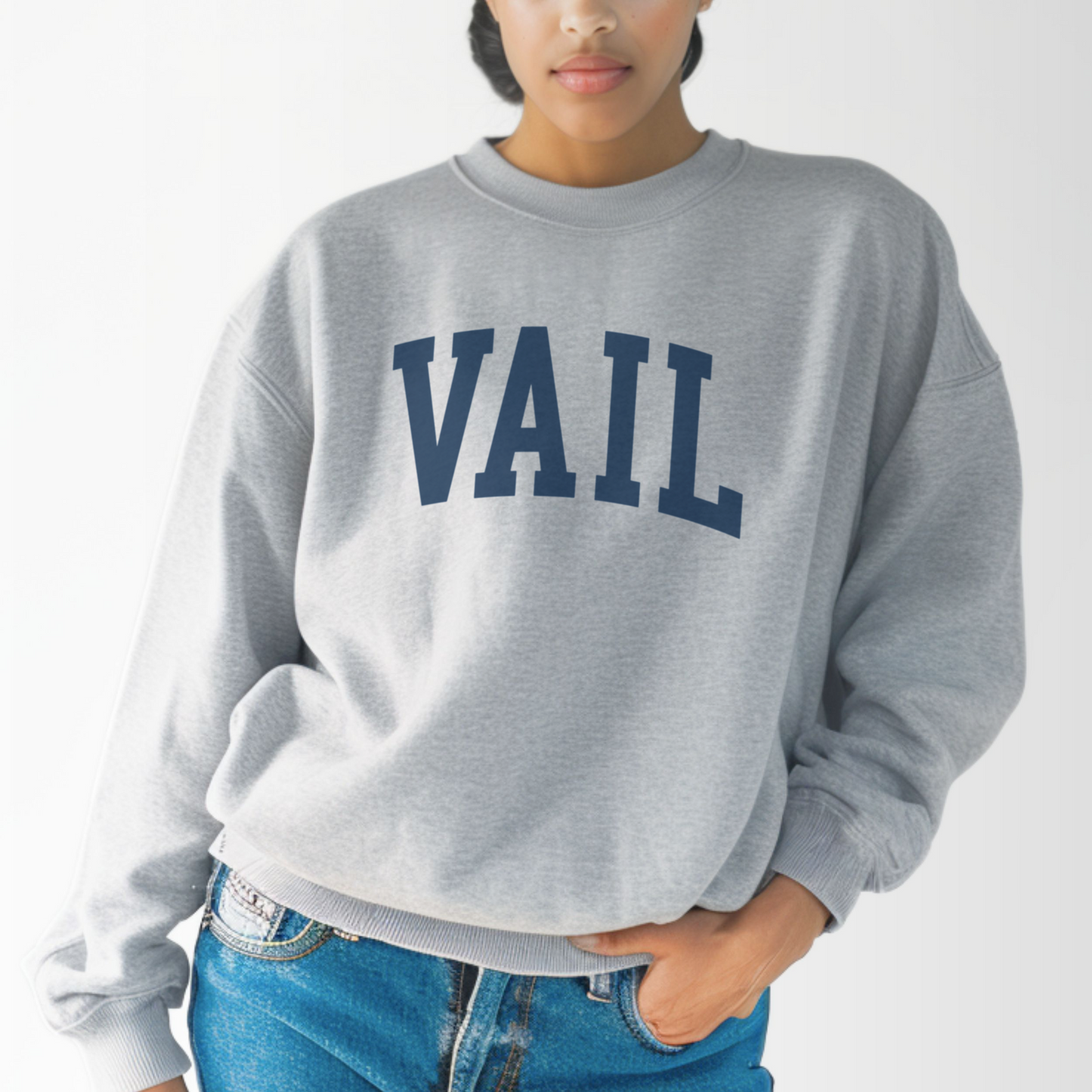 A model wears the Sport Grey Vail Colorado Varsity Crewneck Sweatshirt.  The ﻿Vail Colorado Varsity﻿ graphic is in bold Navy in a Collegiate style.