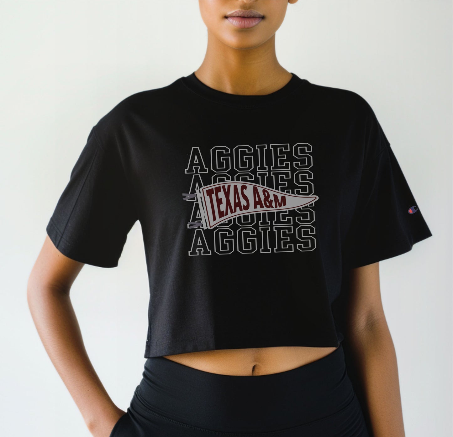 A model wears the Black Adult Womens Texas A&M Aggies Pennant Crop Top.  The ﻿Texas A&M Aggies Pennant﻿ graphic is in bold White in a Varsity style.