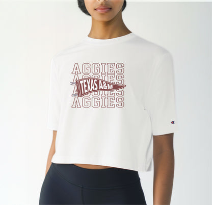 A model wears the White Adult Womens Texas A&M Aggies Pennant Crop Top.  The ﻿Texas A&M Aggies Pennant﻿ graphic is in bold Maroon in a Varsity style.