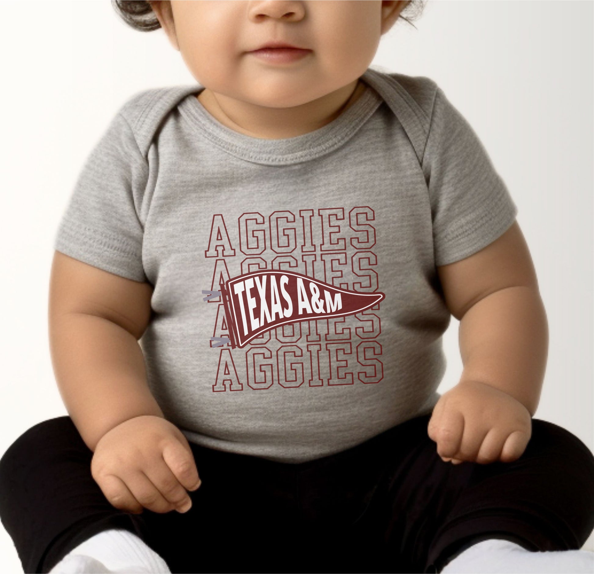 A model wears the Heather Grey Infant Unisex Texas A&M Aggies Pennant Bodysuit.  The ﻿Texas A&M Aggies Pennant﻿ graphic is in bold Maroon in a Varsity style.