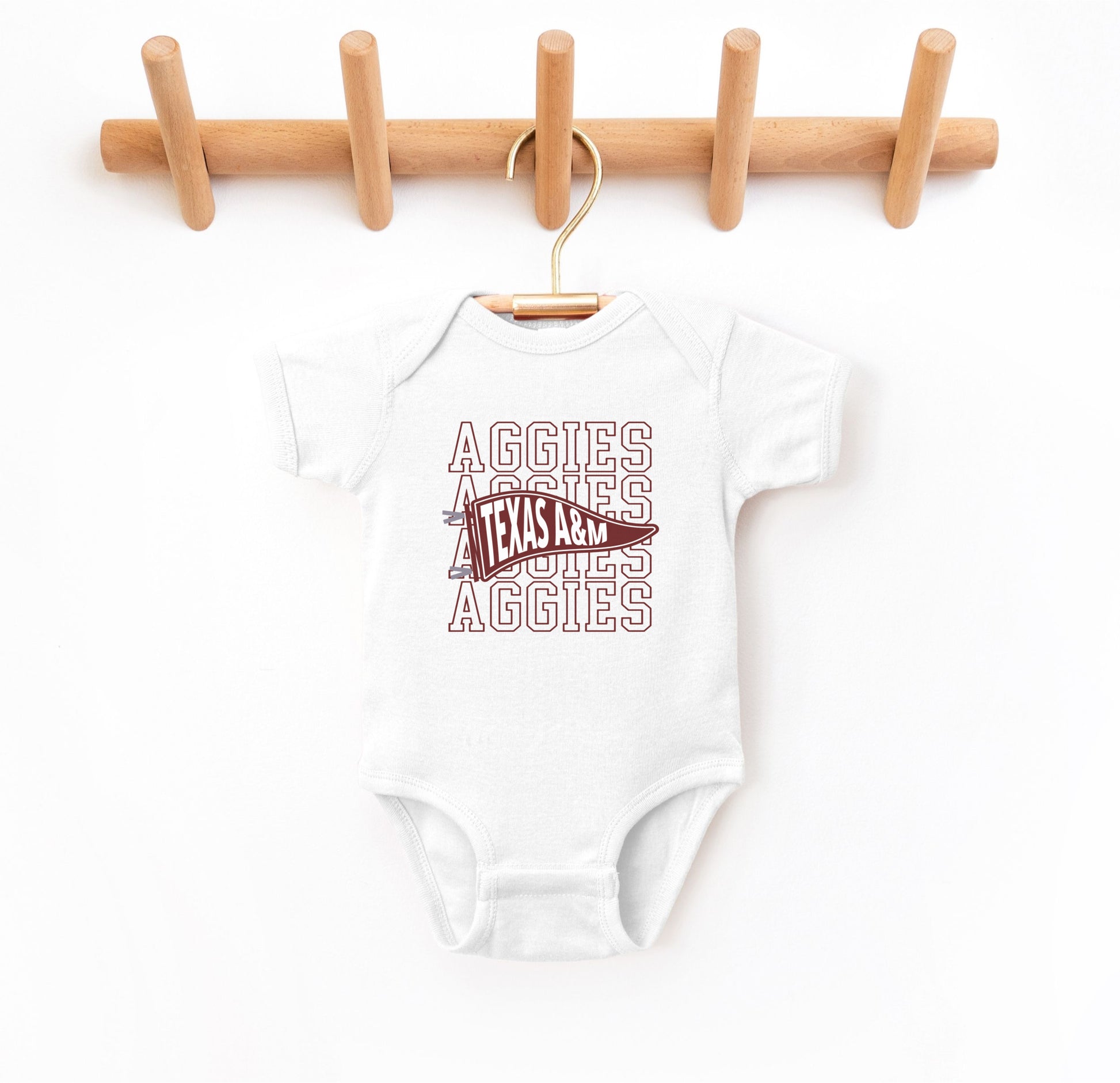 The White Infant Unisex Texas A&M Aggies Pennant Bodysuit lays flat on a white background. The ﻿Texas A&M Aggies Pennant﻿ graphic is in bold Maroon in a Varsity style.