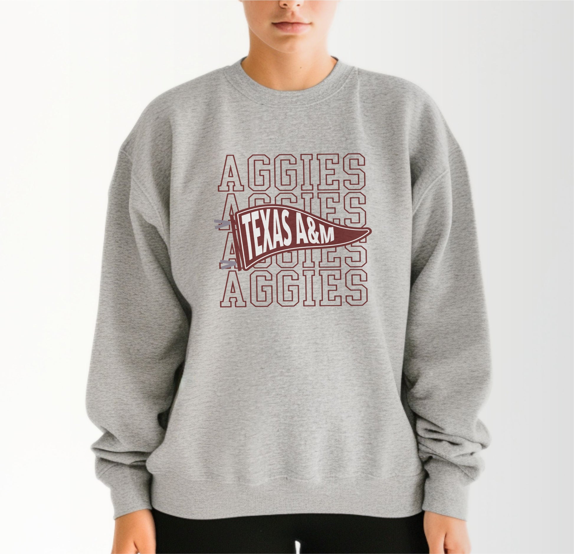 A model wears the Sport Grey Adult Unisex Texas A&M Aggies Pennant Crewneck Sweatshirt.  The ﻿Texas A&M Aggies Pennant﻿ graphic is in bold Maroon in a Varsity style.