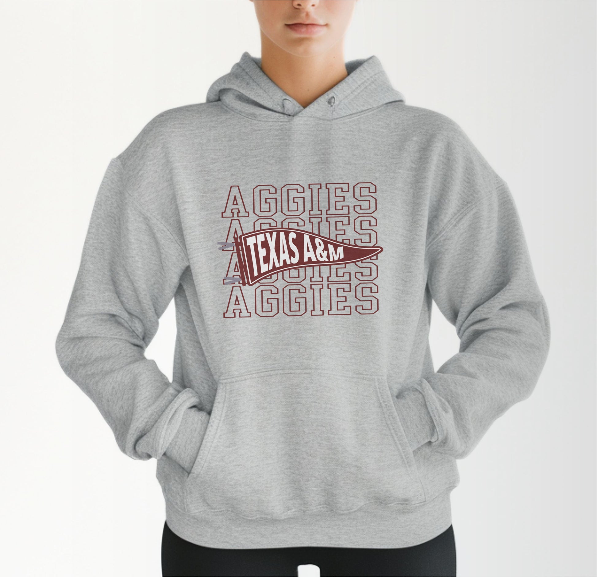 A model wears the Sport Grey Adult Unisex Texas A&M Aggies Pennant Hooded Sweatshirt.  The ﻿Texas A&M Aggies Pennant﻿ graphic is in bold Maroon in a Varsity style.