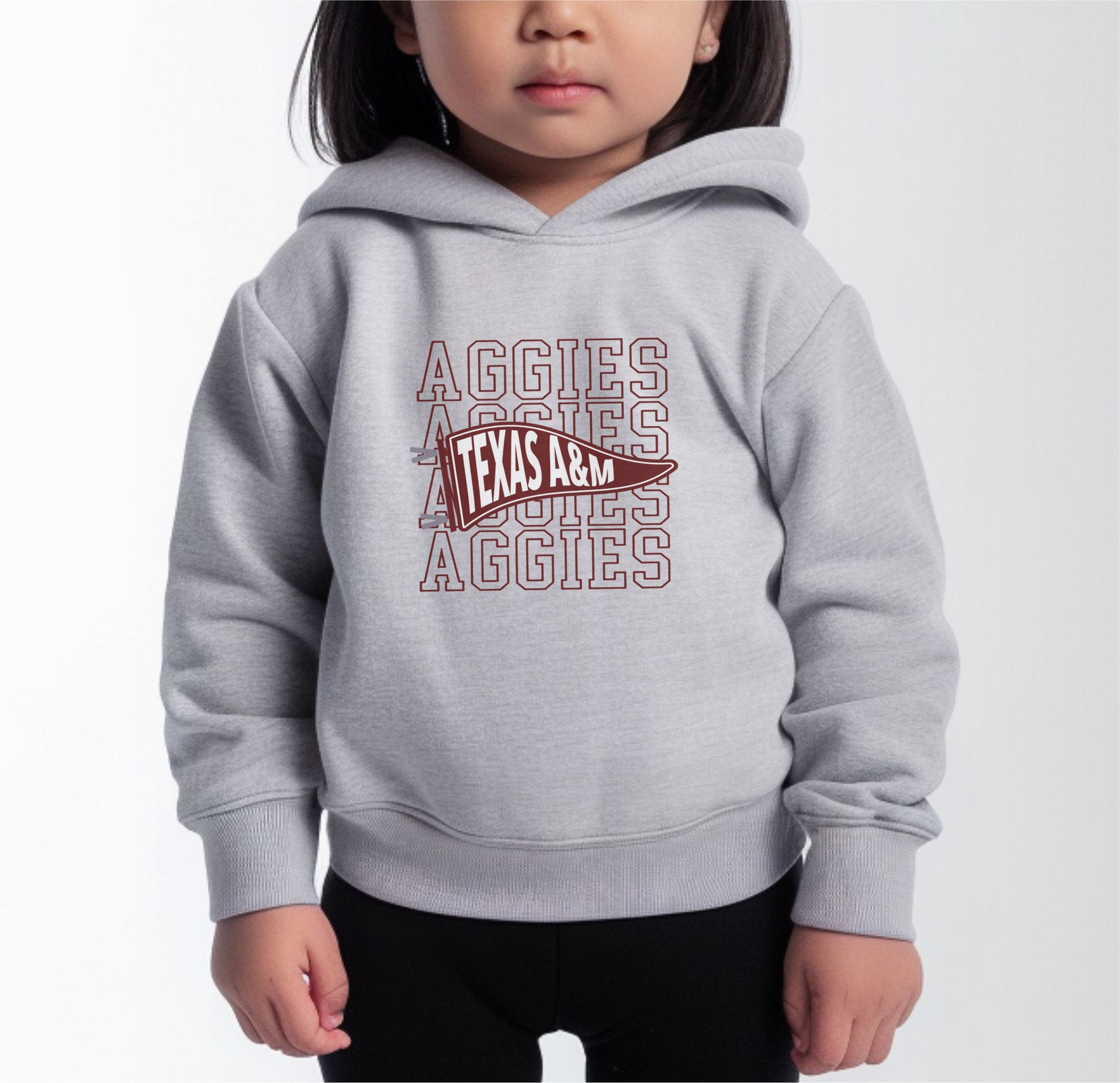 A model wears the Heather Grey Toddler Unisex Texas A&M Aggies Pennant Hooded Sweatshirt.  The ﻿Texas A&M Aggies Pennant﻿ graphic is in bold Maroon in a Varsity style.