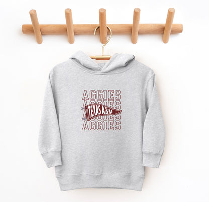 The Heather Grey Toddler Unisex Texas A&M Aggies Pennant Hooded Sweatshirt lays flat on a white background. The ﻿Texas A&M Aggies Pennant﻿ graphic is in bold Maroon in a Varsity style.