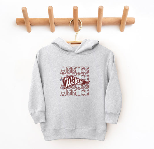 The Heather Grey Toddler Unisex Texas A&M Aggies Pennant Hooded Sweatshirt lays flat on a white background. The ﻿Texas A&M Aggies Pennant﻿ graphic is in bold Maroon in a Varsity style.