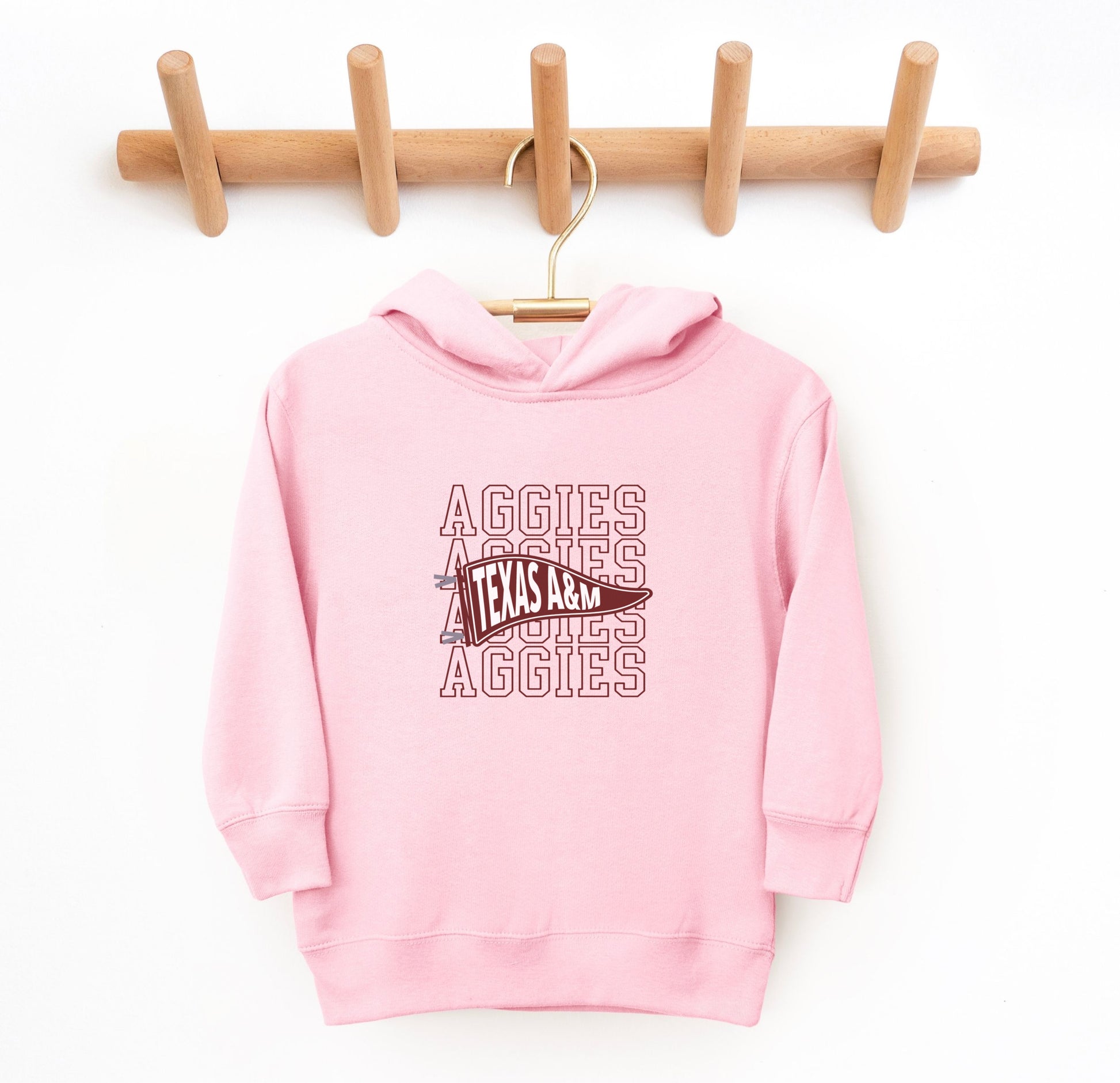 The Pink Toddler Unisex Texas A&M Aggies Pennant Hooded Sweatshirt lays flat on a white background. The ﻿Texas A&M Aggies Pennant﻿ graphic is in bold White in a Varsity style.