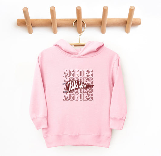 The Pink Toddler Unisex Texas A&M Aggies Pennant Hooded Sweatshirt lays flat on a white background. The ﻿Texas A&M Aggies Pennant﻿ graphic is in bold White in a Varsity style.