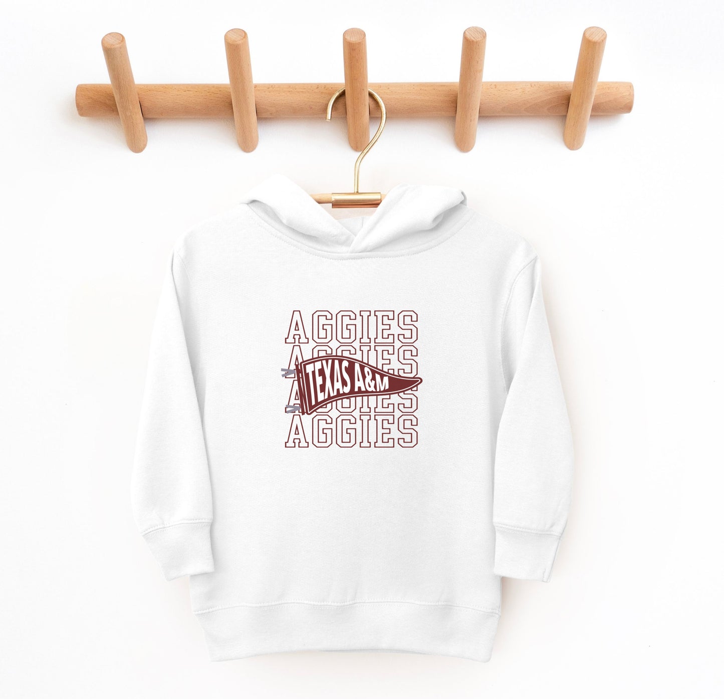 The White Toddler Unisex Texas A&M Aggies Pennant Hooded Sweatshirt lays flat on a white background. The ﻿Texas A&M Aggies Pennant﻿ graphic is in bold Maroon in a Varsity style.