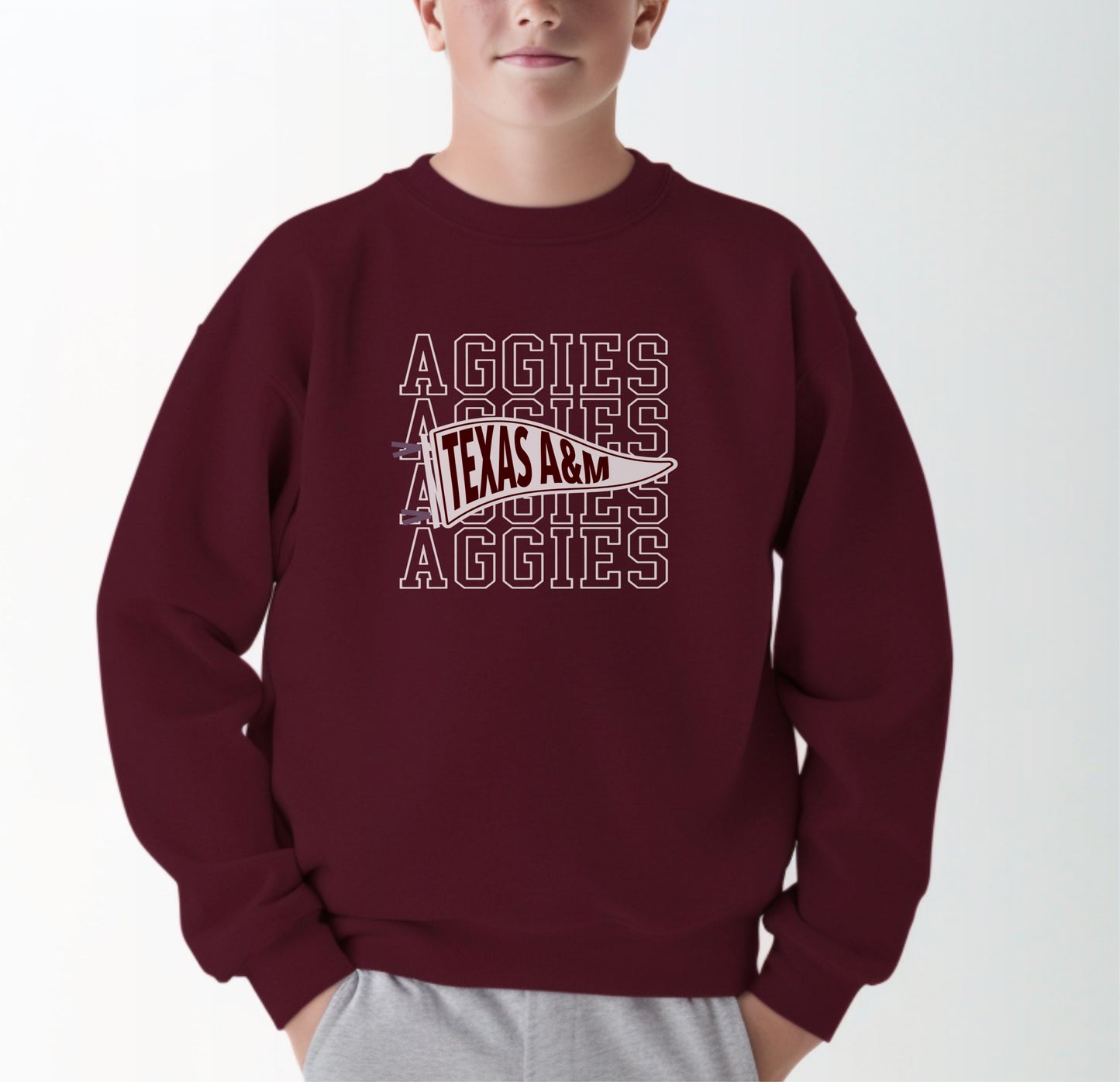 A model wears the Maroon Youth Unisex Texas A&M Aggies Pennant Crewneck Sweatshirt.  The ﻿Texas A&M Aggies Pennant﻿ graphic is in bold White in a Varsity style.