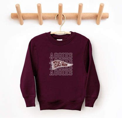 The Maroon Youth Unisex Texas A&M Aggies Pennant Crewneck Sweatshirt lays flat on a white background. The ﻿Texas A&M Aggies Pennant﻿ graphic is in bold White in a Varsity style.