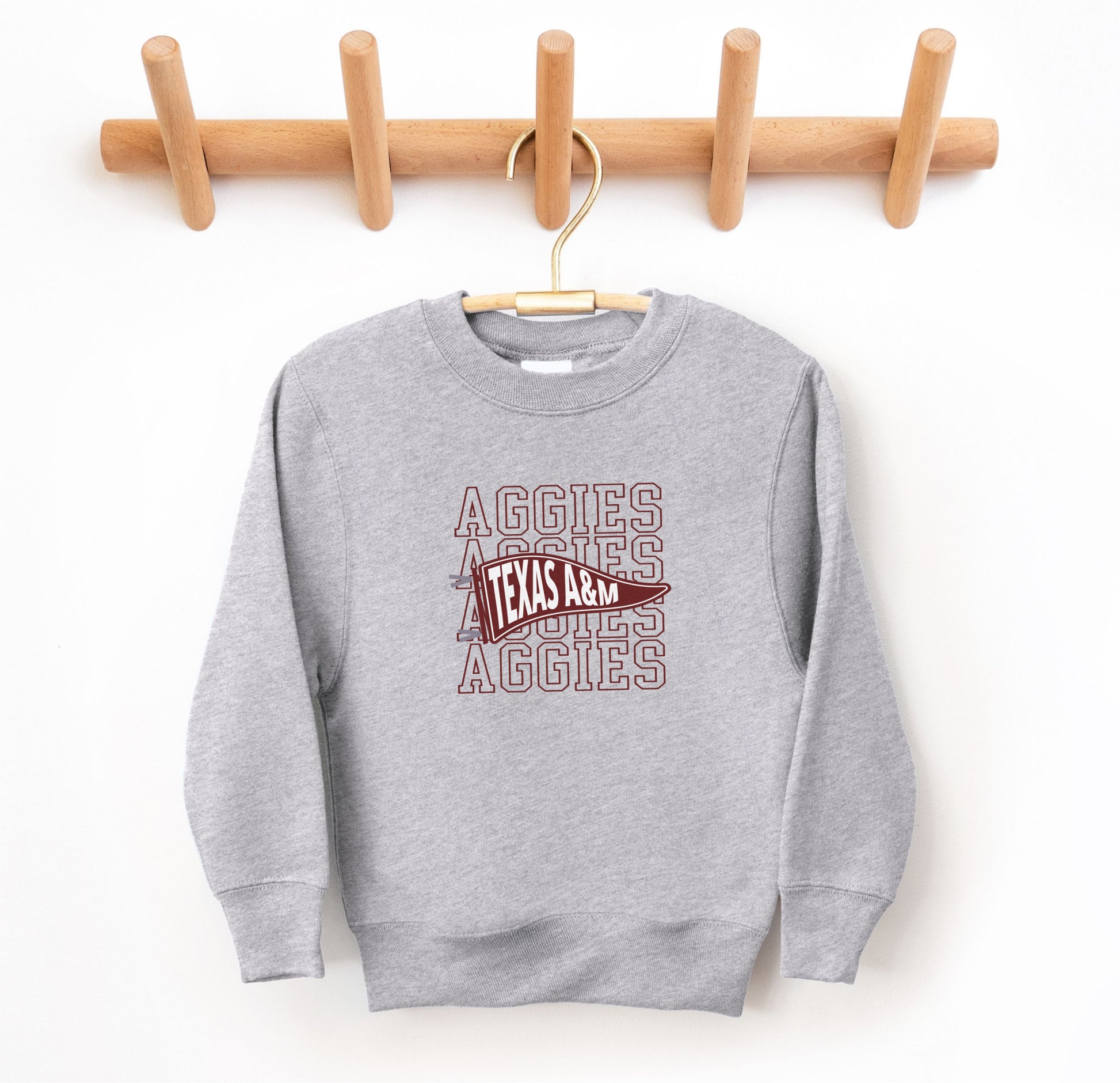 The Sport Grey Youth Unisex Texas A&M Aggies Pennant Crewneck Sweatshirt lays flat on a white background. The ﻿Texas A&M Aggies Pennant﻿ graphic is in bold Maroon in a Varsity style.