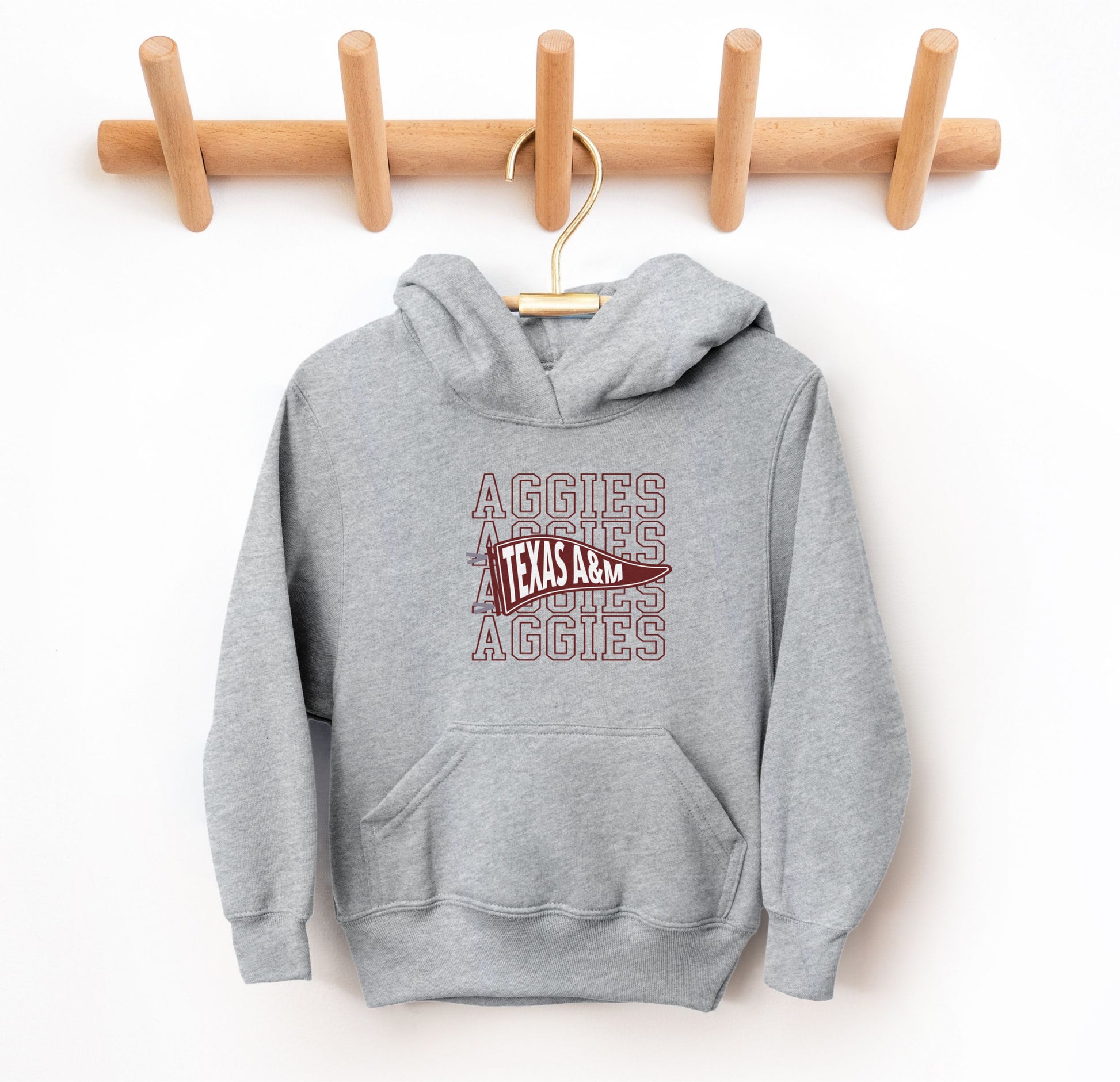 The Sport Grey Youth Unisex Texas A&M Aggies Pennant Hooded Sweatshirt lays flat on a white background. The ﻿Texas A&M Aggies Pennant﻿ graphic is in bold Maroon in a Varsity style.