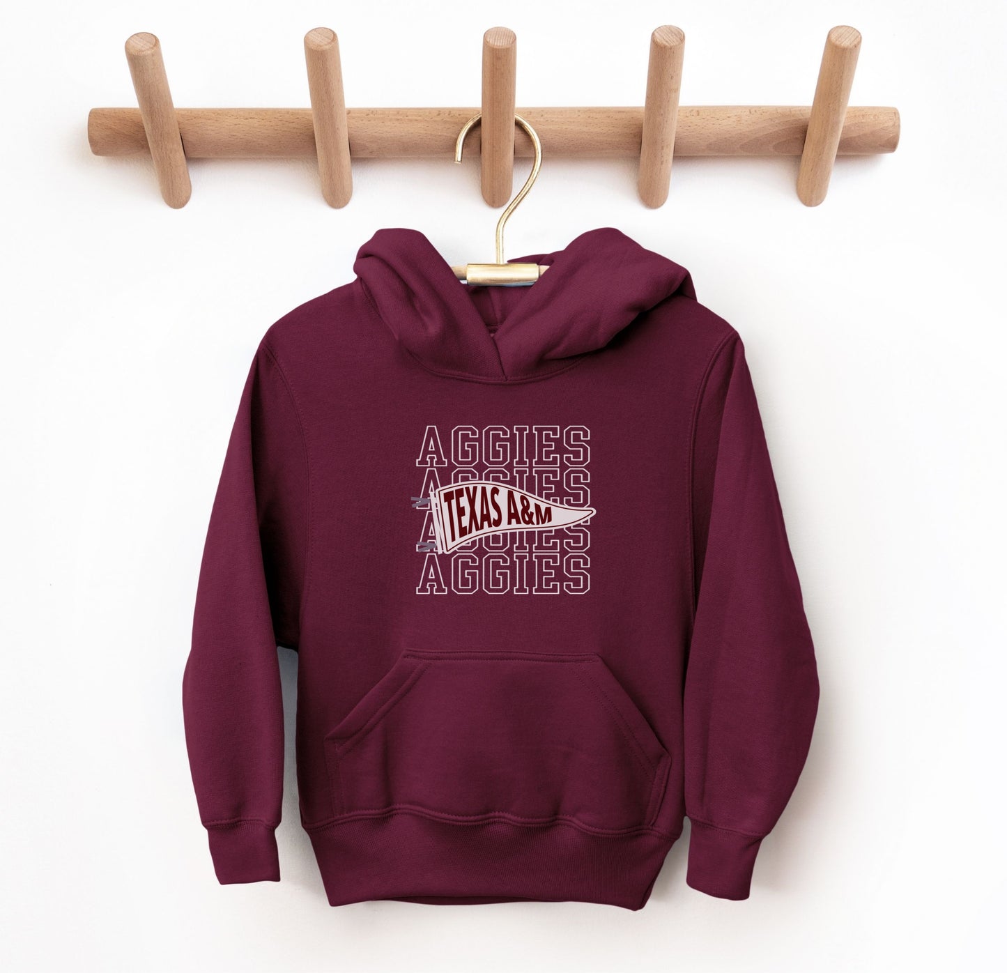 The Maroon Youth Unisex Texas A&M Aggies Pennant Hooded Sweatshirt lays flat on a white background. The ﻿Texas A&M Aggies Pennant﻿ graphic is in bold White in a Varsity style.