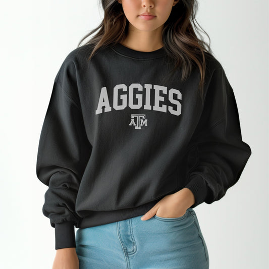 A model wears the Black Adult Unisex Texas A&M Aggies Collegiate Crewneck Sweatshirt.  The ﻿Texas A&M Aggies Collegiate﻿ graphic is in bold White in a Varsity style.