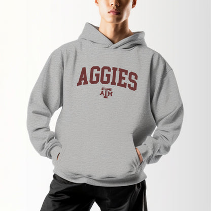 A model wears the Sport Grey Adult Unisex Texas A&M Aggies Collegiate Hooded Sweatshirt.  The ﻿Texas A&M Aggies Collegiate﻿ graphic is in bold Maroon in a Varsity style.