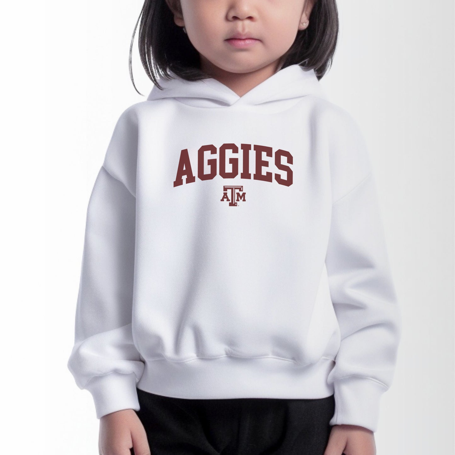 A model wears the White Toddler Unisex Texas A&M Aggies Collegiate Hooded Sweatshirt.  The ﻿Texas A&M Aggies Collegiate﻿ graphic is in bold Maroon in a Varsity style.