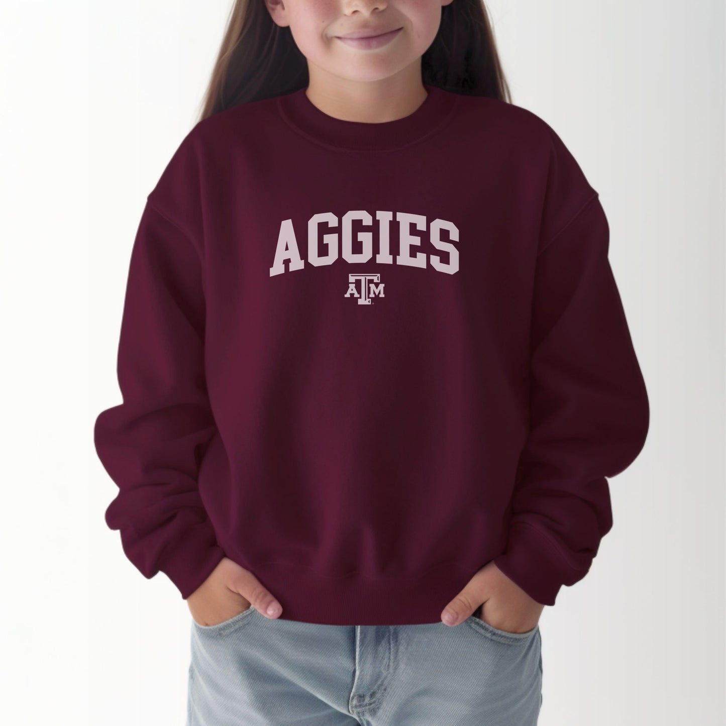 A model wears the Maroon Youth Unisex Texas A&M Aggies Collegiate Crewneck Sweatshirt.  The ﻿Texas A&M Aggies Collegiate﻿ graphic is in bold White in a Varsity style.