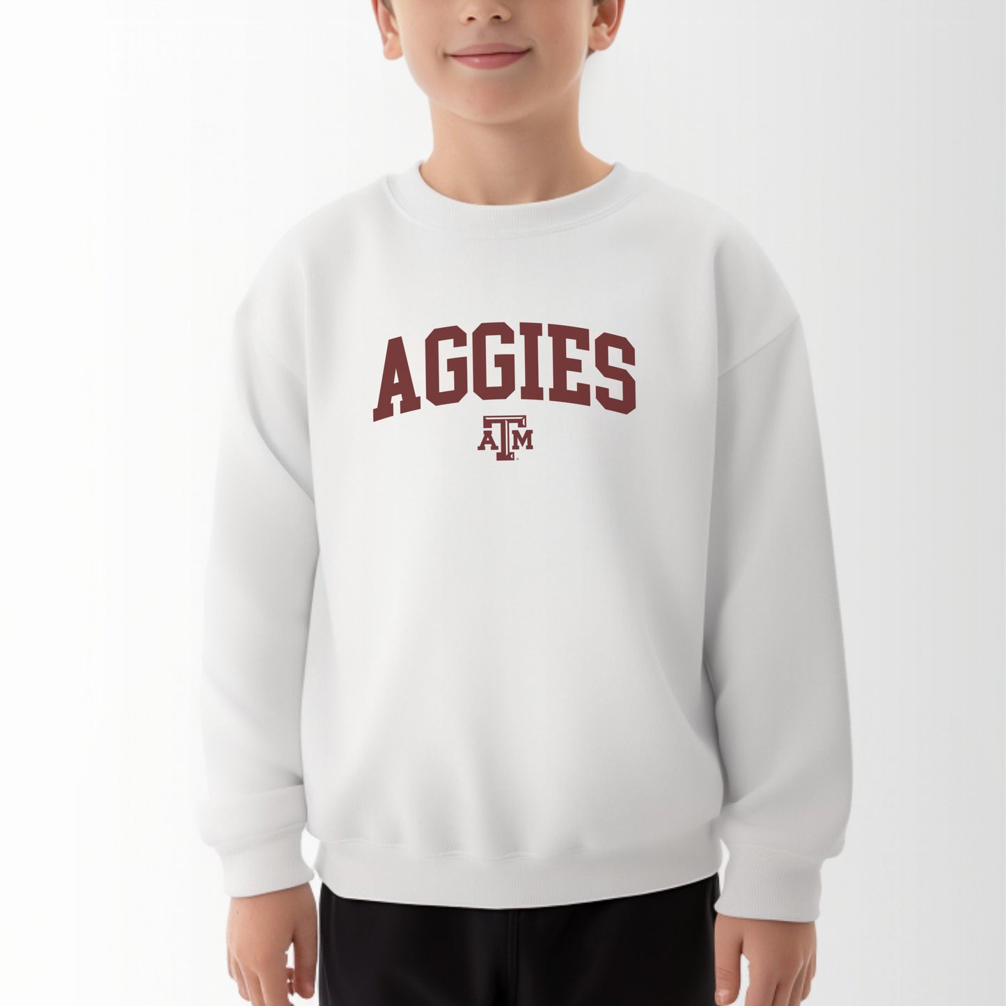 A model wears the White Youth Unisex Texas A&M Aggies Collegiate Crewneck Sweatshirt.  The ﻿Texas A&M Aggies Collegiate﻿ graphic is in bold Maroon in a Varsity style.