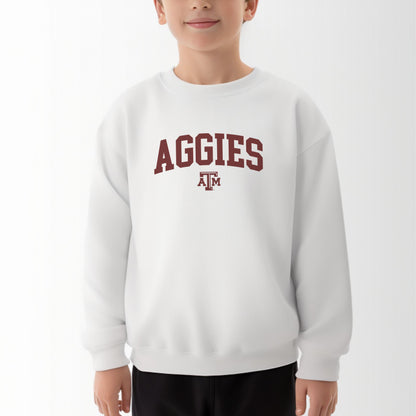 A model wears the White Youth Unisex Texas A&M Aggies Collegiate Crewneck Sweatshirt.  The ﻿Texas A&M Aggies Collegiate﻿ graphic is in bold Maroon in a Varsity style.