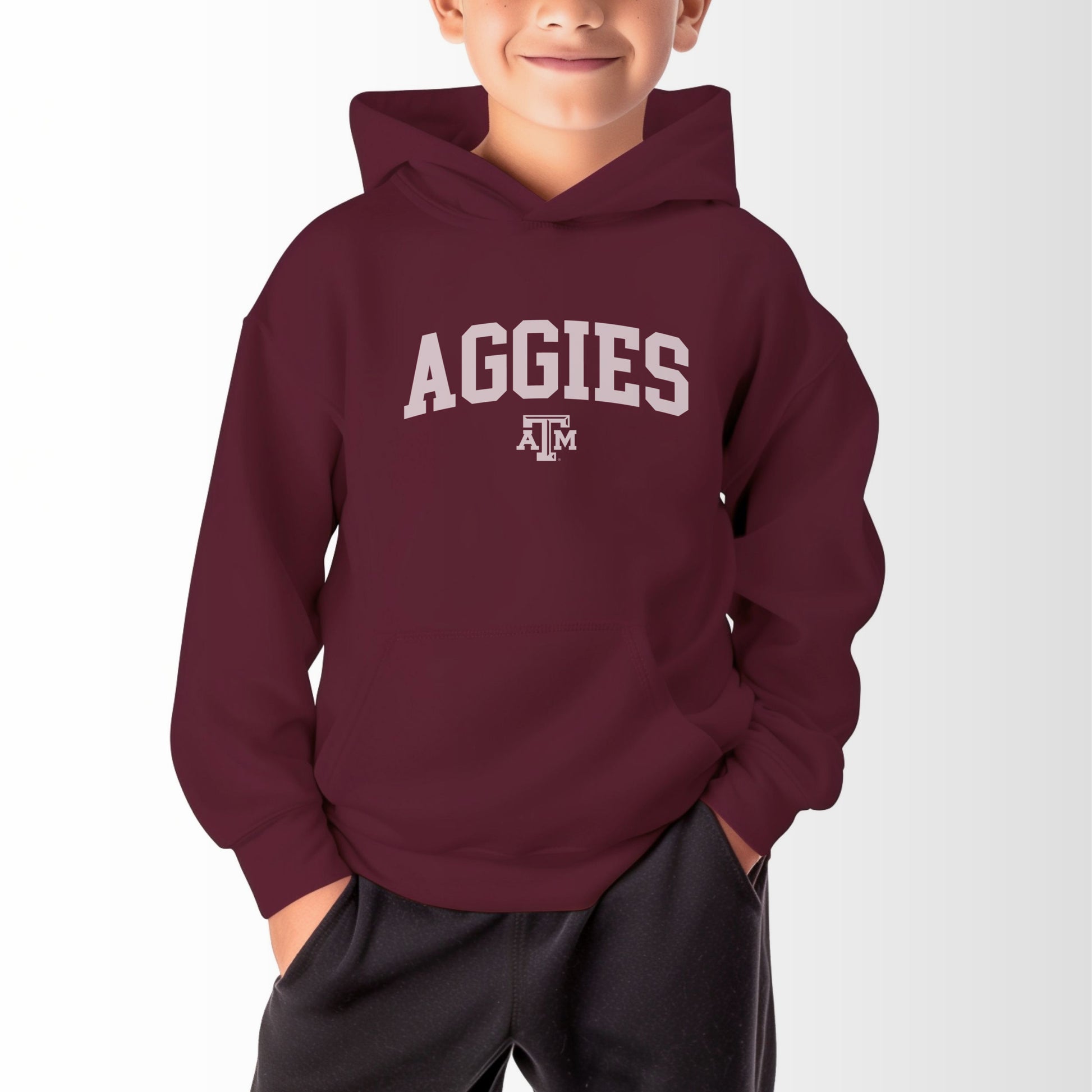 A model wears the Maroon Youth Unisex Texas A&M Aggies Collegiate Hooded Sweatshirt.  The ﻿Texas A&M Aggies Collegiate﻿ graphic is in bold White in a Varsity style.