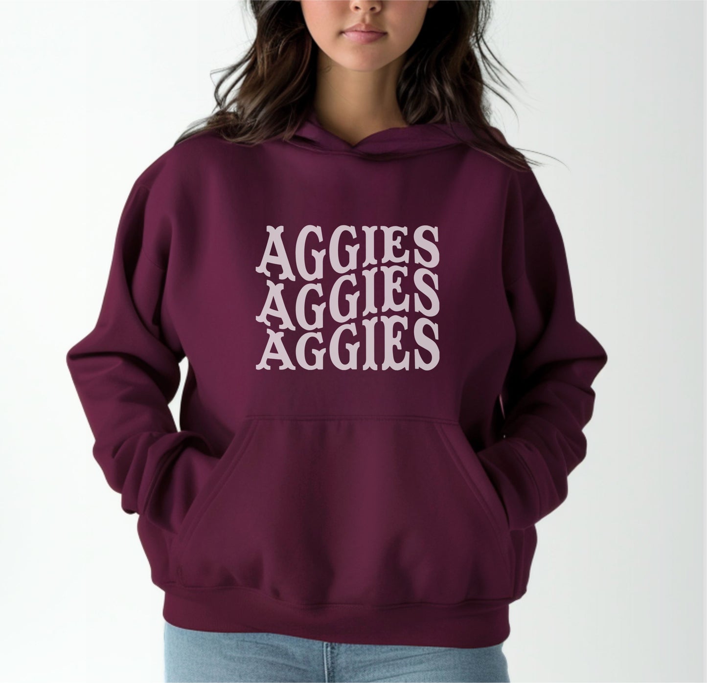 A model wears the Maroon Adult Unisex Texas A&M Aggies Aggies Aggies Western Hooded Sweatshirt.  The ﻿Texas A&M Aggies Aggies Aggies Western﻿ graphic is in bold White in a Western style.