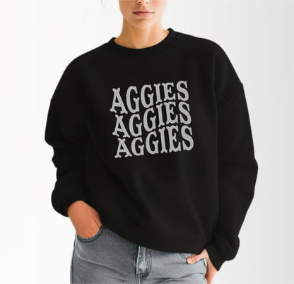 A model wears the Black Adult Unisex Texas A&M Aggies Aggies Aggies Western Crewneck Sweatshirt.  The ﻿Texas A&M Aggies Aggies Aggies Western﻿ graphic is in bold White in a Western style.