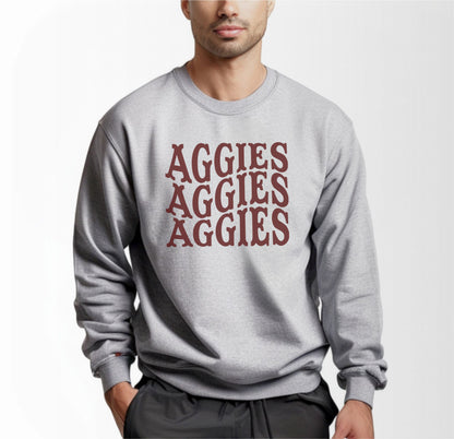 A model wears the Sport Grey Adult Unisex Texas A&M Aggies Aggies Aggies Western Crewneck Sweatshirt.  The ﻿Texas A&M Aggies Aggies Aggies Western﻿ graphic is in bold Maroon in a Western style.