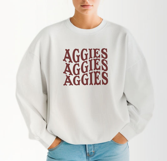 A model wears the White Adult Unisex Texas A&M Aggies Aggies Aggies Western Crewneck Sweatshirt.  The ﻿Texas A&M Aggies Aggies Aggies Western﻿ graphic is in bold Maroon in a Western style.