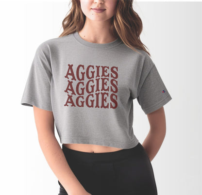 A model wears the Oxford Grey Adult Womens Texas A&M Aggies Aggies Aggies Western Crop Top.  The ﻿Texas A&M Aggies Aggies Aggies Western﻿ graphic is in bold Maroon in a Western style.