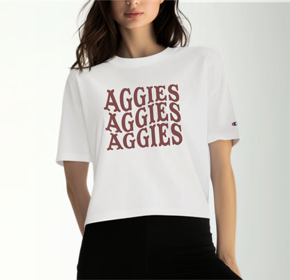 A model wears the White Adult Womens Texas A&M Aggies Aggies Aggies Western Crop Top.  The ﻿Texas A&M Aggies Aggies Aggies Western﻿ graphic is in bold Maroon in a Western style.