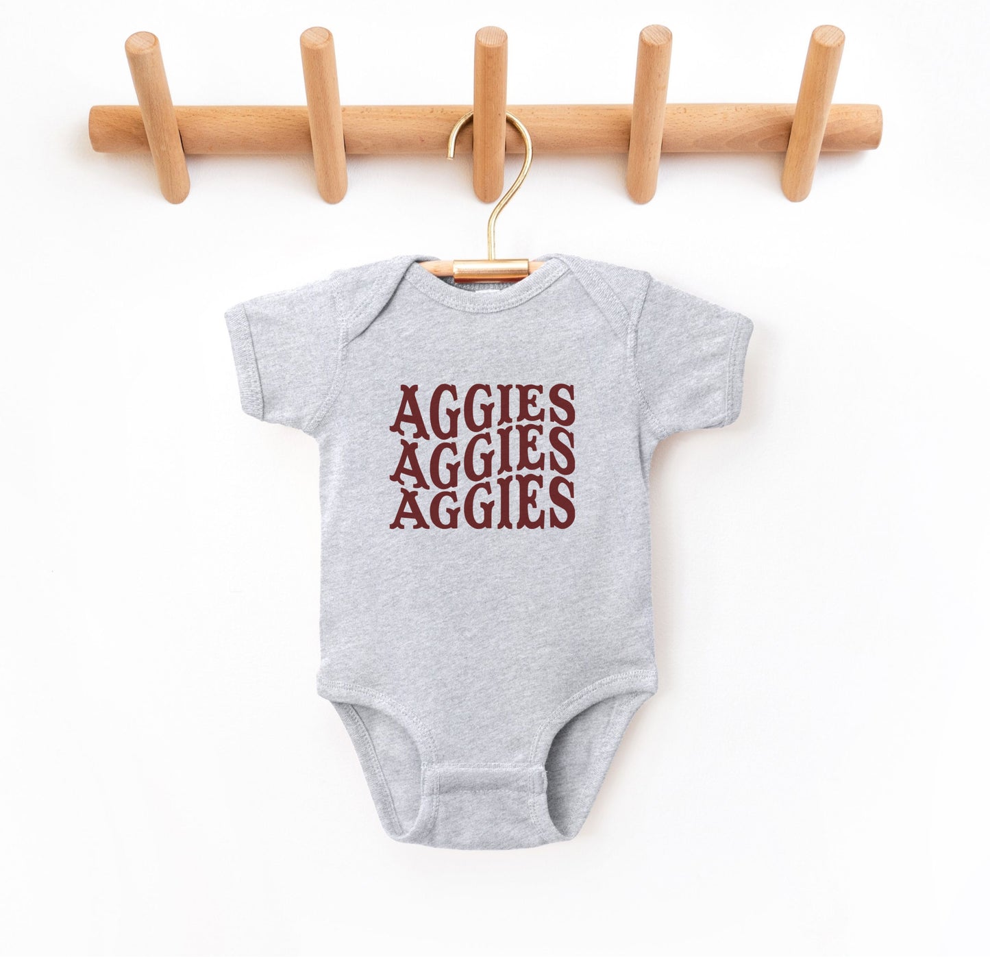 The Heather Grey Infant Unisex Texas A&M Aggies Aggies Aggies Western Bodysuit lays flat on a white background. The ﻿Texas A&M Aggies Aggies Aggies Western﻿ graphic is in bold Maroon in a Western style.