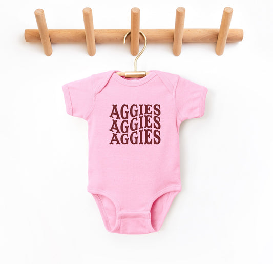 The Pink Infant Unisex Texas A&M Aggies Aggies Aggies Western Bodysuit lays flat on a white background. The ﻿Texas A&M Aggies Aggies Aggies Western﻿ graphic is in bold Maroon in a Western style.