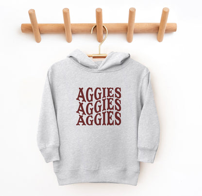 The Heather Grey Toddler Unisex Texas A&M Aggies Aggies Aggies Western Hooded Sweatshirt lays flat on a white background. The ﻿Texas A&M Aggies Aggies Aggies Western﻿ graphic is in bold Maroon in a Western style.