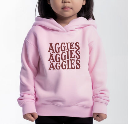 A model wears the Pink Toddler Unisex Texas A&M Aggies Aggies Aggies Western Hooded Sweatshirt.  The ﻿Texas A&M Aggies Aggies Aggies Western﻿ graphic is in bold White in a Western style.