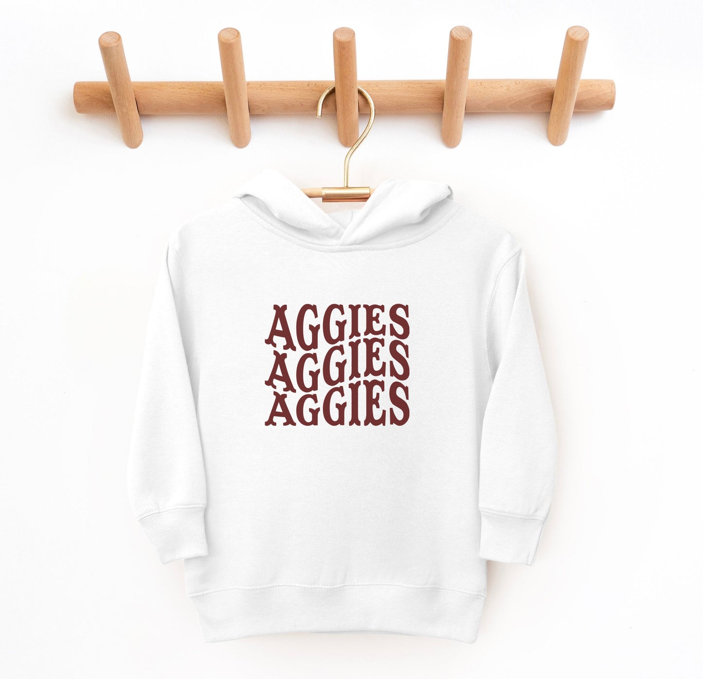 The White Toddler Unisex Texas A&M Aggies Aggies Aggies Western Hooded Sweatshirt lays flat on a white background. The ﻿Texas A&M Aggies Aggies Aggies Western﻿ graphic is in bold Maroon in a Western style.