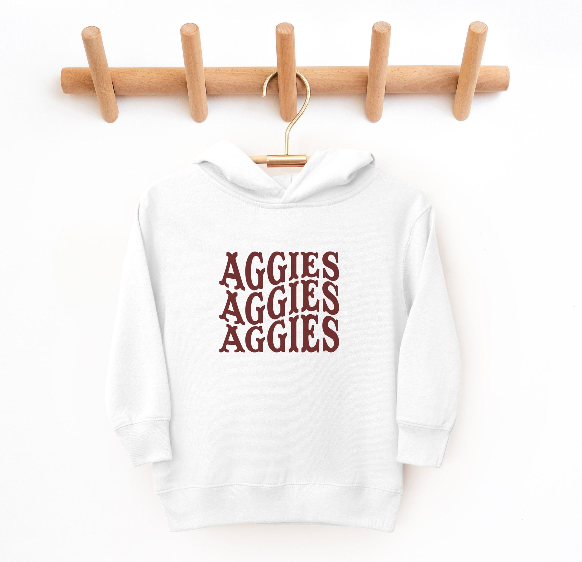 The White Toddler Unisex Texas A&M Aggies Aggies Aggies Western Hooded Sweatshirt lays flat on a white background. The ﻿Texas A&M Aggies Aggies Aggies Western﻿ graphic is in bold Maroon in a Western style.