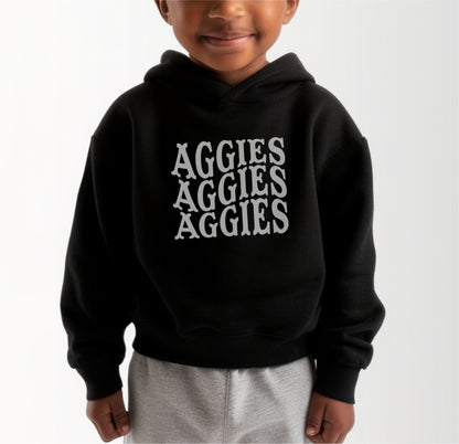 A model wears the Black Toddler Unisex Texas A&M Aggies Aggies Aggies Western Hooded Sweatshirt.  The ﻿Texas A&M Aggies Aggies Aggies Western﻿ graphic is in bold White in a Western style.